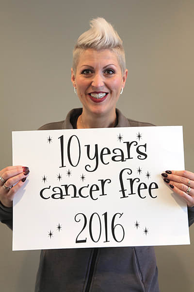 Heather holds a sign celebrating 10 years cancer free, 2016.