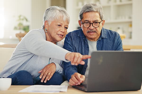 Senior man and woman looking at a laptop and paperwork together, with one person pointing at the computer screen