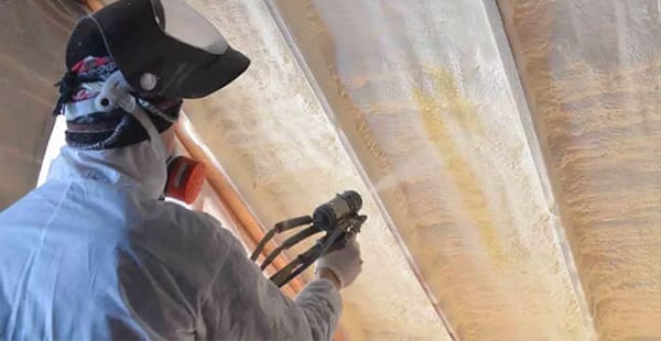 Photo of a worker spraying fireproofing foam on the underside of a roof