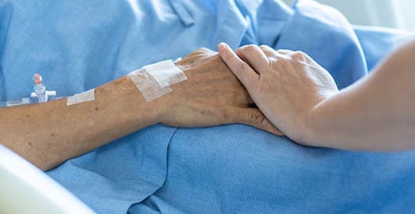 An image of a loved one's hand clasping a mesothelioma patient's hand as it rests on a blue hospital bed