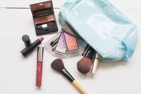Makeup bag and cosmetics scattered on a vanity, including brushes, lipstick and palettes.