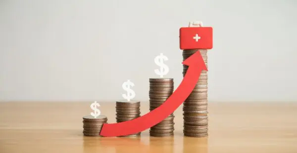 Stacks of coins growing taller with dollar signs and medical kit, symbolizing rising costs of mesothelioma treatment