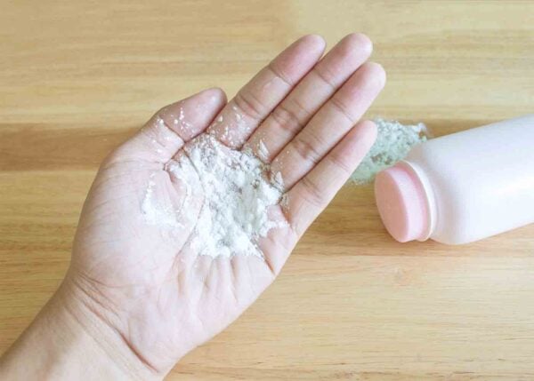 An image of a hand holding talcum powder, with a bottle of talcum powder on a surface in the background