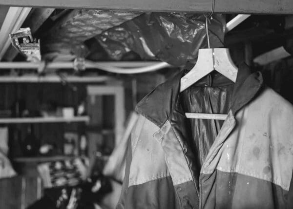 This image depicts a dirty work jacket hanging in a basement. It has dusty areas that could be asbestos fiber residue. It represents a common mode of secondary asbestos exposure in which an individual who works with asbestos inadvertently carries it home with them on their clothing or other work gear.