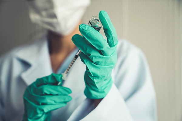 A masked doctor wearing green gloves uses a small syringe to withdraw an experimental cancer vaccine from a glass vial. The vaccine will be part of a mesothelioma treatment regimen.