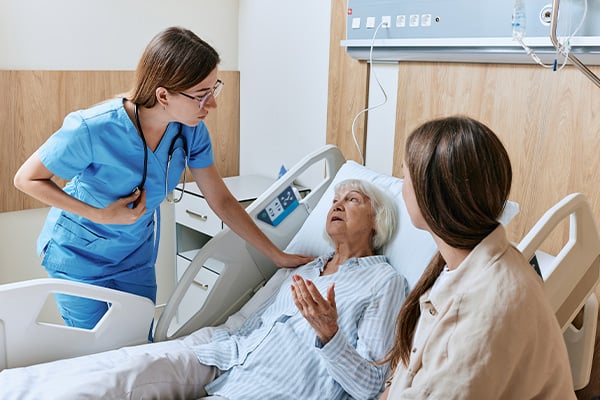 A patient in a hospital bed with their caregiver and a member of their healthcare team attending to them