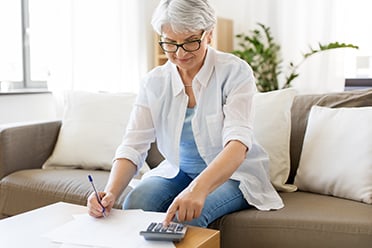Image of woman calculating expenses with a calculator and pen and paper
