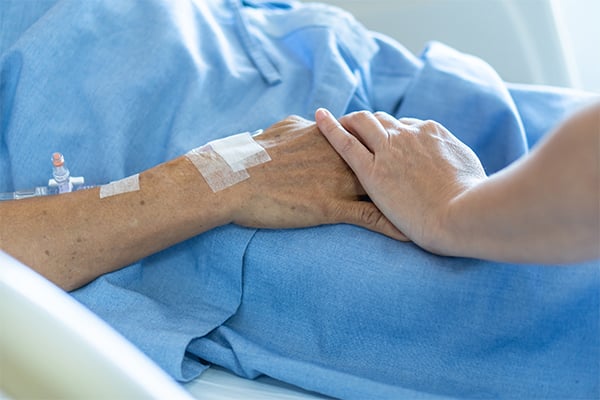 An image of a loved one's hand clasping a mesothelioma patient's hand as it rests on a blue hospital bed
