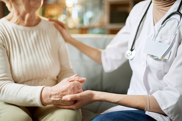 Doctor and mesothelioma patient holding hands while discussing palliative care.