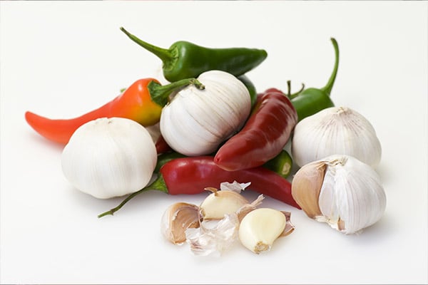 This image shows a few garlic bunches in a pile with several chili peppers (orange, red and green). Both garlic and chili peppers may be beneficial for lung health.
