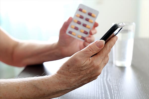 A picture of a mesothelioma patient's hand holding a smartphone to use an app to track his medications he holds in his other hand.