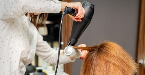 Hairdresser blow drying hair. Old hair dryers were once made with asbestos, creating an exposure risk.