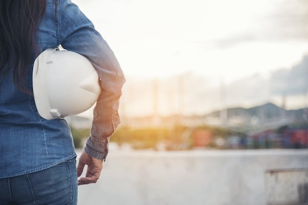 A woman who works in construction stands on the edge of a sunlit build site. Women like her may be at risk of asbestos exposure, which can cause malignant mesothelioma.