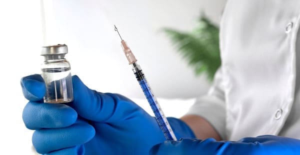 Medical professional wearing surgical gloves holding a syringe and vaccine vial