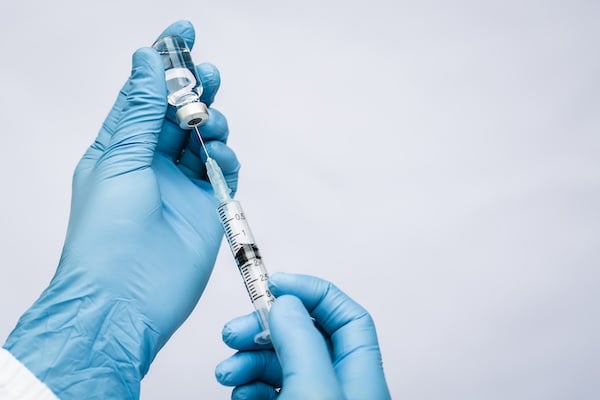 A doctor wearing blue gloves uses a small syringe to extract immunotherapy from a vial