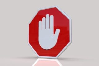 A large stop sign bearing a centered hand icon sits in the center of a white room with a white floor, reminding viewers that data shows asbestos should be banned.